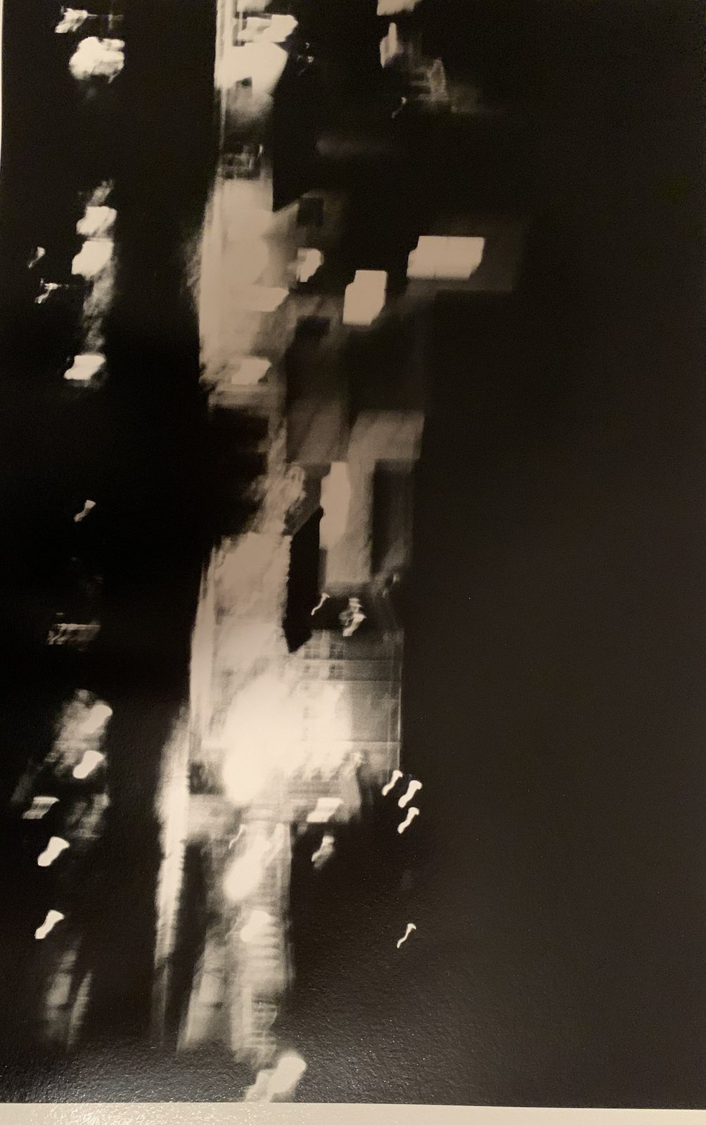 Abstract black-and-white print of blurred city lights and dark building masses