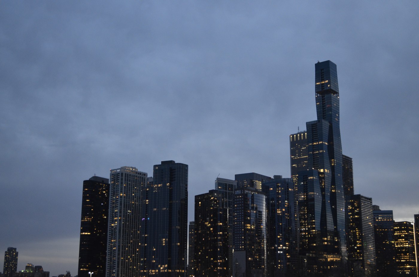 The Chicago skyline lit up at dusk under a cloudy sky