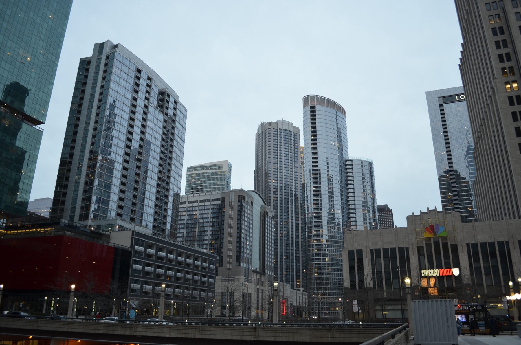 Curved glass residential towers beside a stone building with the NBC peacock logo, at dusk