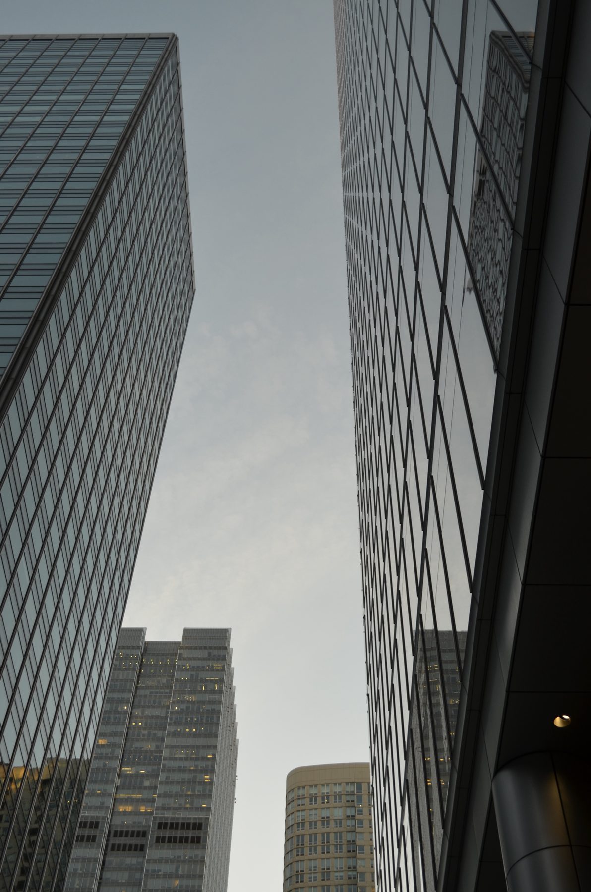 Looking up between two glass towers with a beige tower in the distance